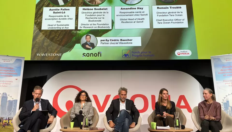 Image capturant tous les intervenants de la conférence assis autours de tables basses. Le logo Veolia est visible en fond et au dessus est projeté la présentation des intervenants 